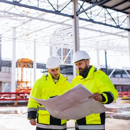 Şantiye sahasında proje planını inceleyen iki teknisyen