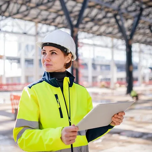 A female engineer in a hard hat working on a tablet at a construction site